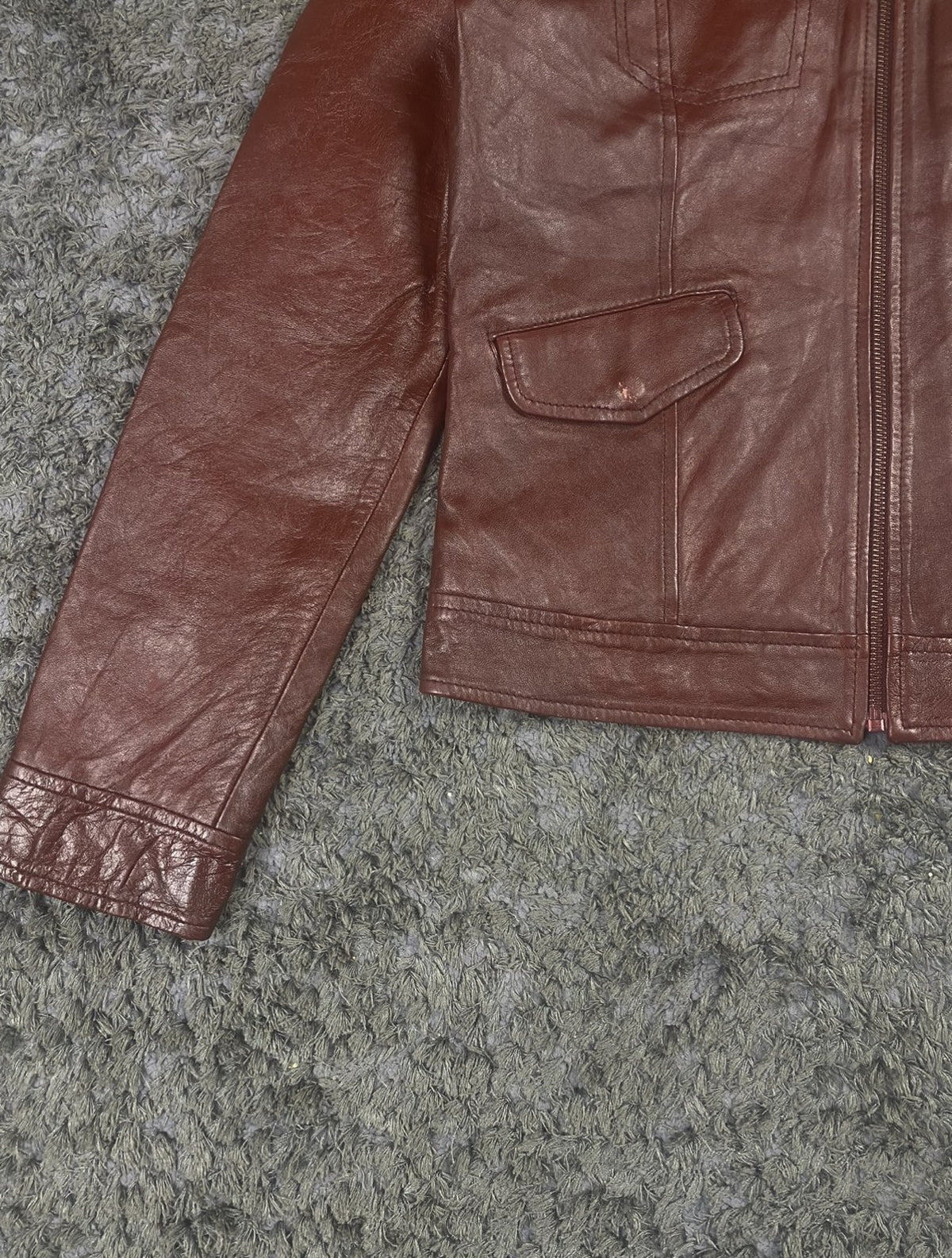 Close view of a front pocket and the straight hem on the burgundy bomber