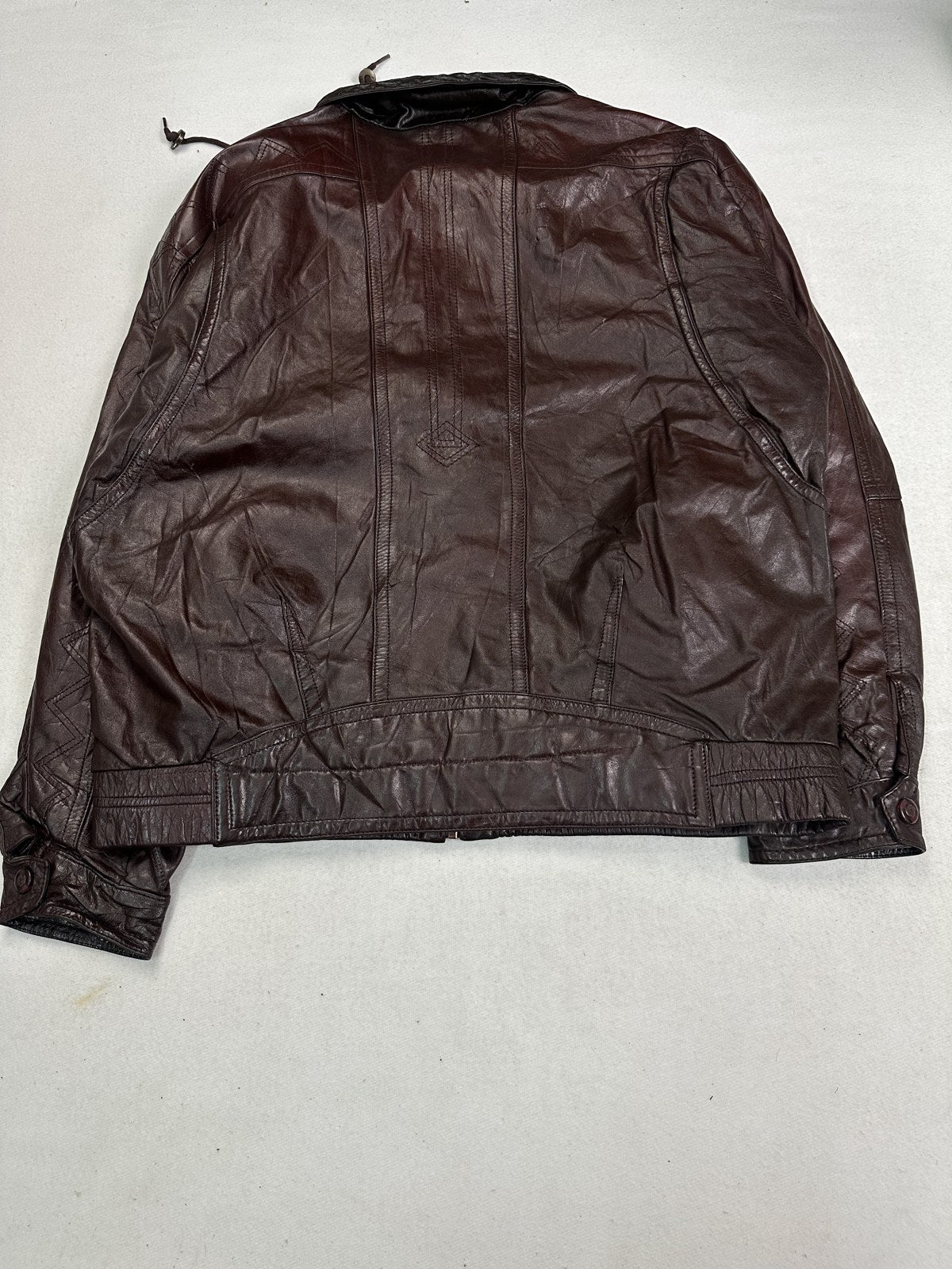 Close detail of the knitted rib hem and side seam on the burgundy bomber jacket