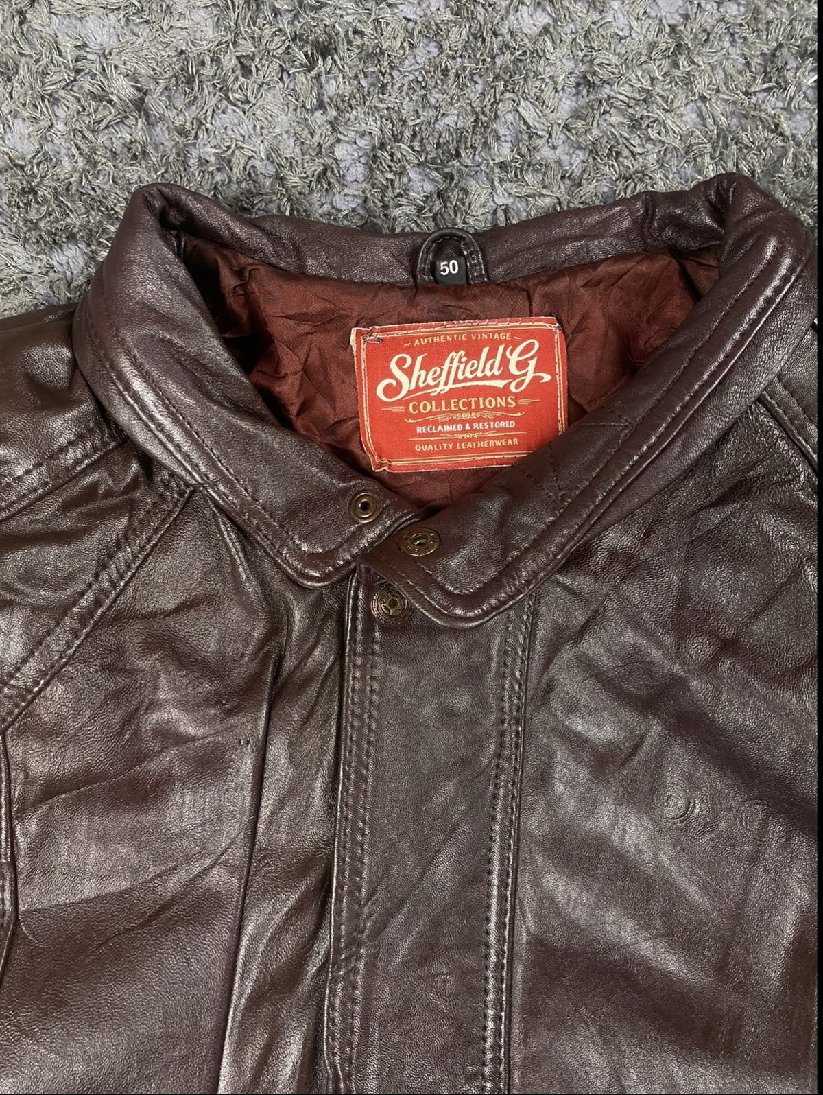 Band collar at the neck of the burgundy leather bomber jacket
