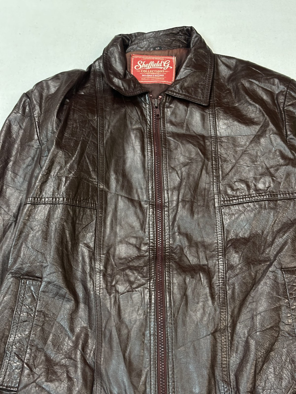 Closer frame of the front of the size M burgundy bomber jacket, band collar and zip in view