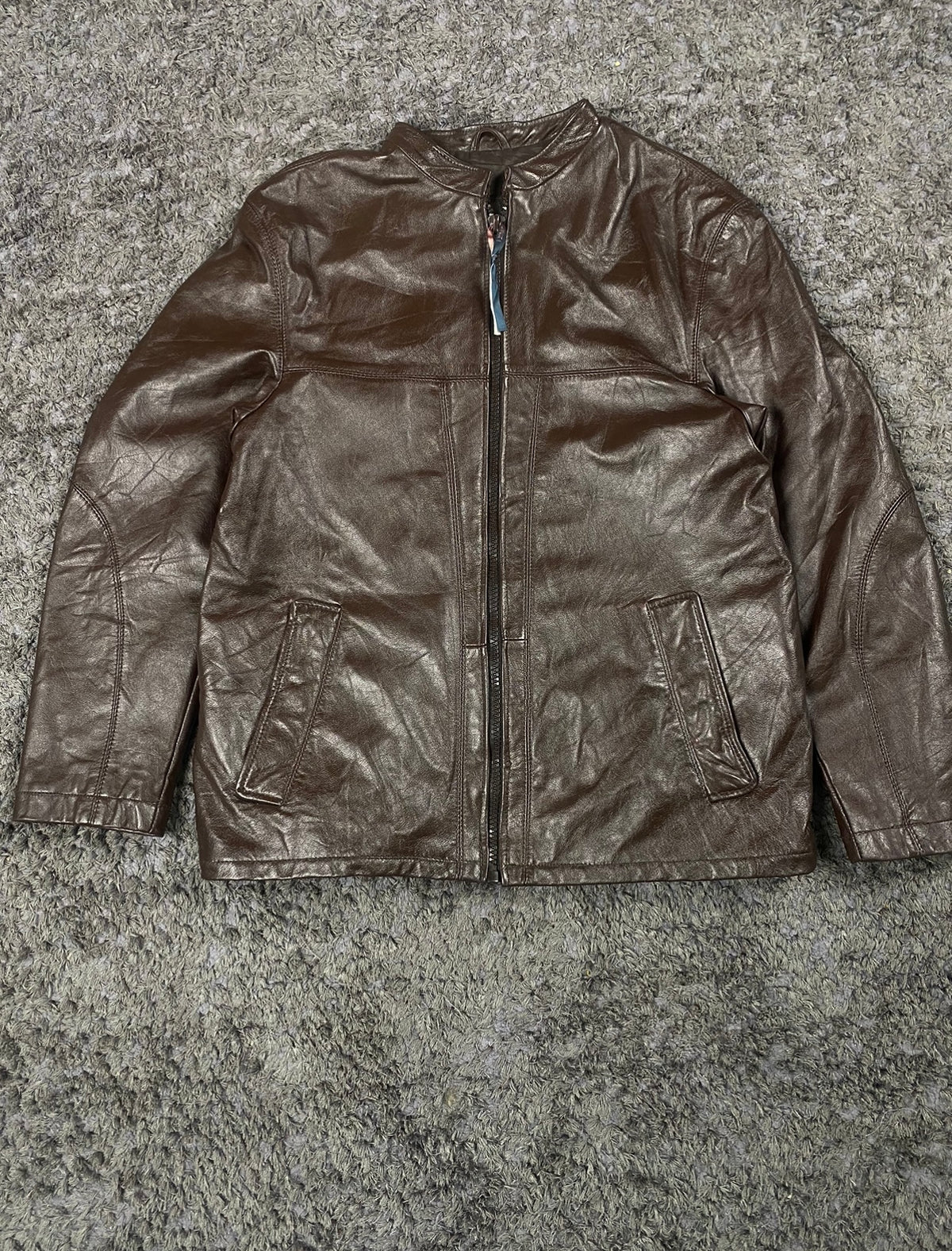 Front of the brown leather jacket laid out flat with both welt hand pockets in view