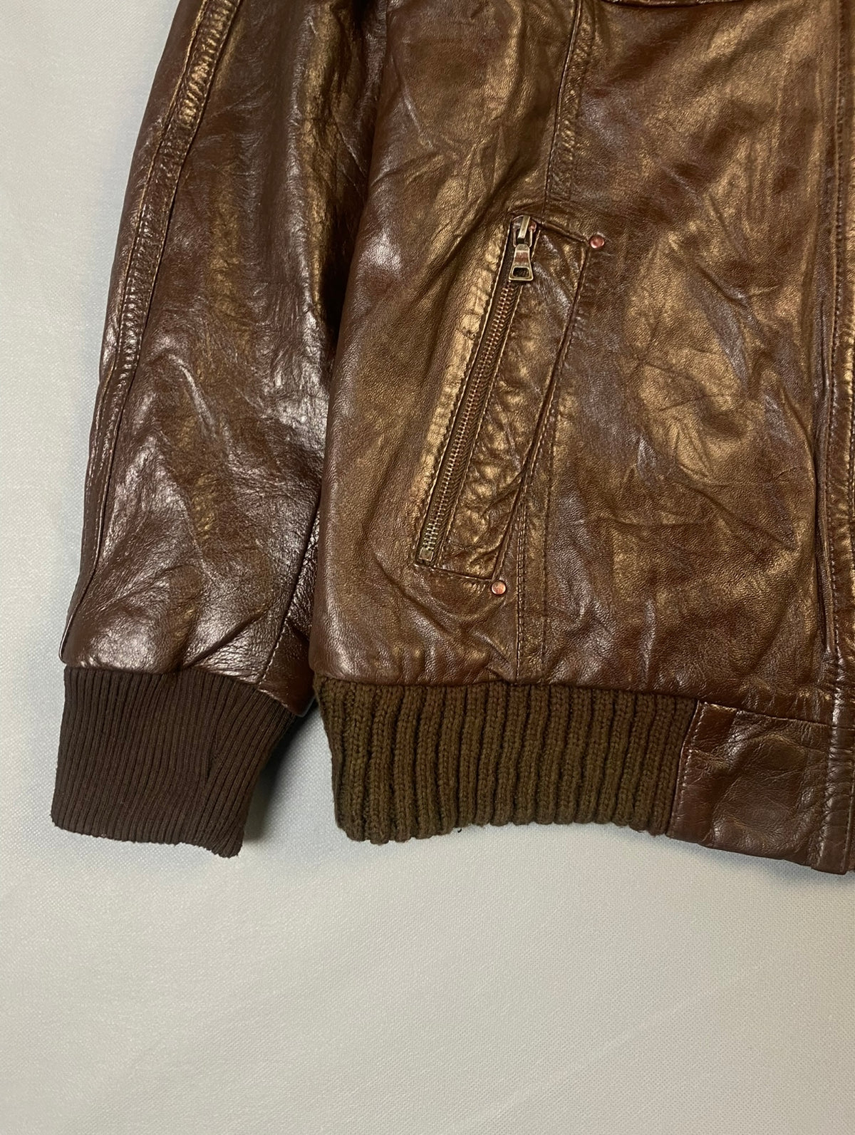 Ribbed cuff and hem beside a slanted zip hand pocket on the brown leather bomber