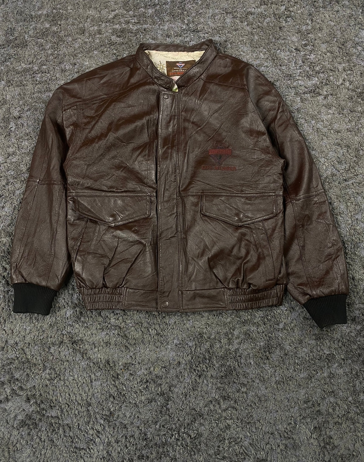 Front of the brown flight jacket zipped up, showing its band collar and ribbed cuffs